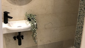 A bathroom with a round mirror, a white sink, and a shower with mosaic tiles.