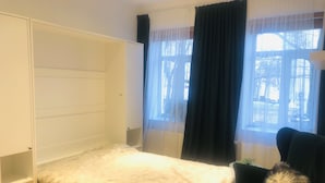 A bedroom with a bed, a chair, a wardrobe, and a window with curtains.