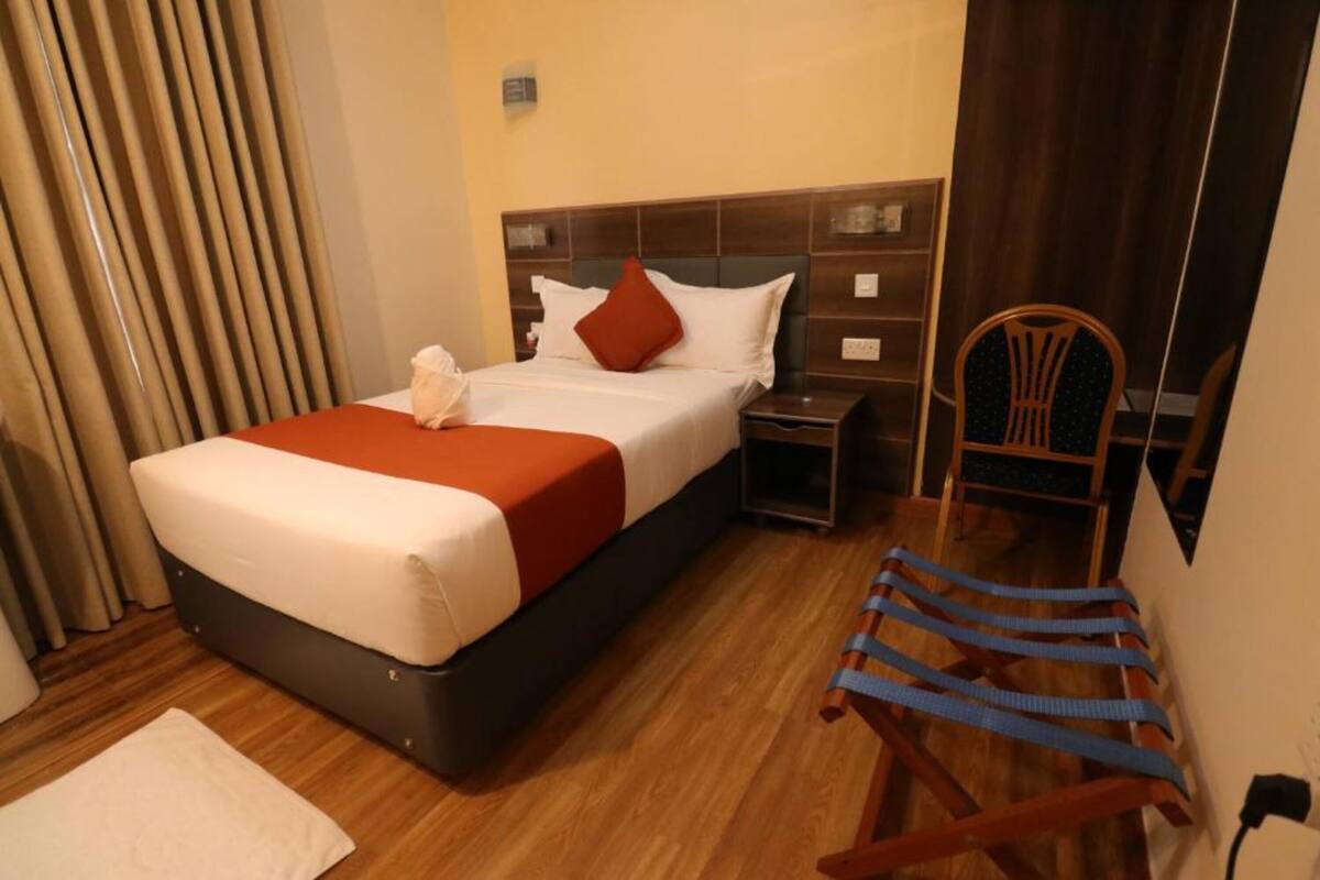Una habitación de hotel con cama, mesita de noche, silla y suelo de madera.