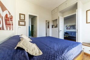 A bedroom with a large bed, a wardrobe, a door leading to a bathroom, and a seating area with a sofa and table. - GuestHost - Bright and quiet apartment of 50 square meters, can accommodate up to 4 people, located on the eighth floor of a building with elevator ( reaches the seventh floor - NOT suitable for disabled people).The property boasts an amazing view of Rom (Roma)