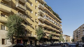 Um edifício residencial com várias andares, varandas, carros estacionados e árvores.