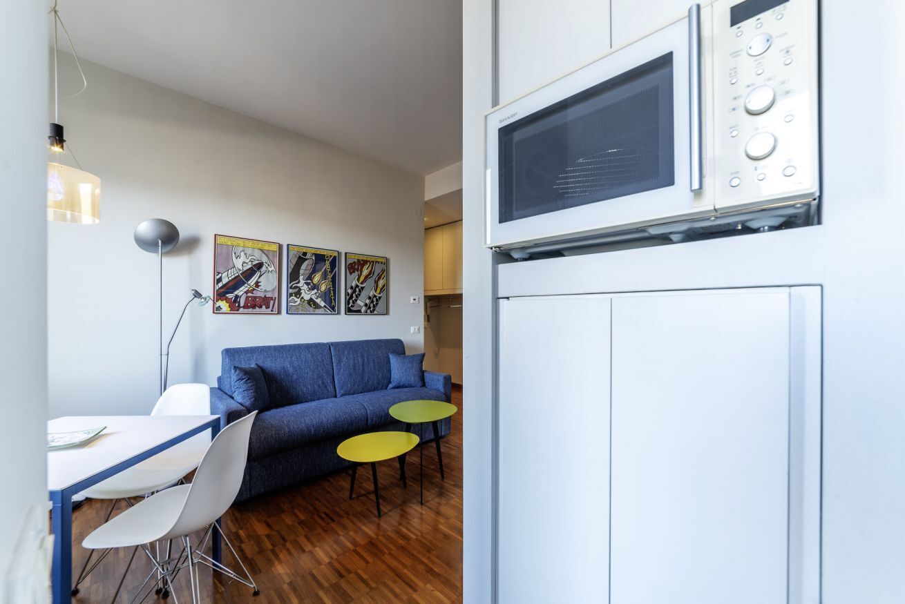 A modern kitchen with a microwave, a dining area with a blue sofa and two small tables, and a wall with framed artwork.