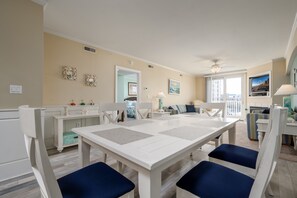 A dining area with a white table and blue cushioned chairs, beige walls, and a ceiling fan.