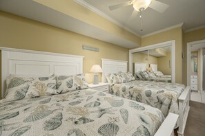 A bedroom with two beds, a ceiling fan, a mirror, and a nightstand with a lamp.