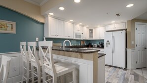 A kitchen with white cabinets, a central island with bar stools, a microwave, a refrigerator, and a sink. - Beautifully decorated, 3 bedroom, 3 bath condo in great mid town location (Ocean City)