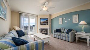 A living room with striped sofas, a white coffee table, a ceiling fan, a fireplace, and a view through a sliding glass door. - Beautifully decorated, 3 bedroom, 3 bath condo in great mid town location (Ocean City)