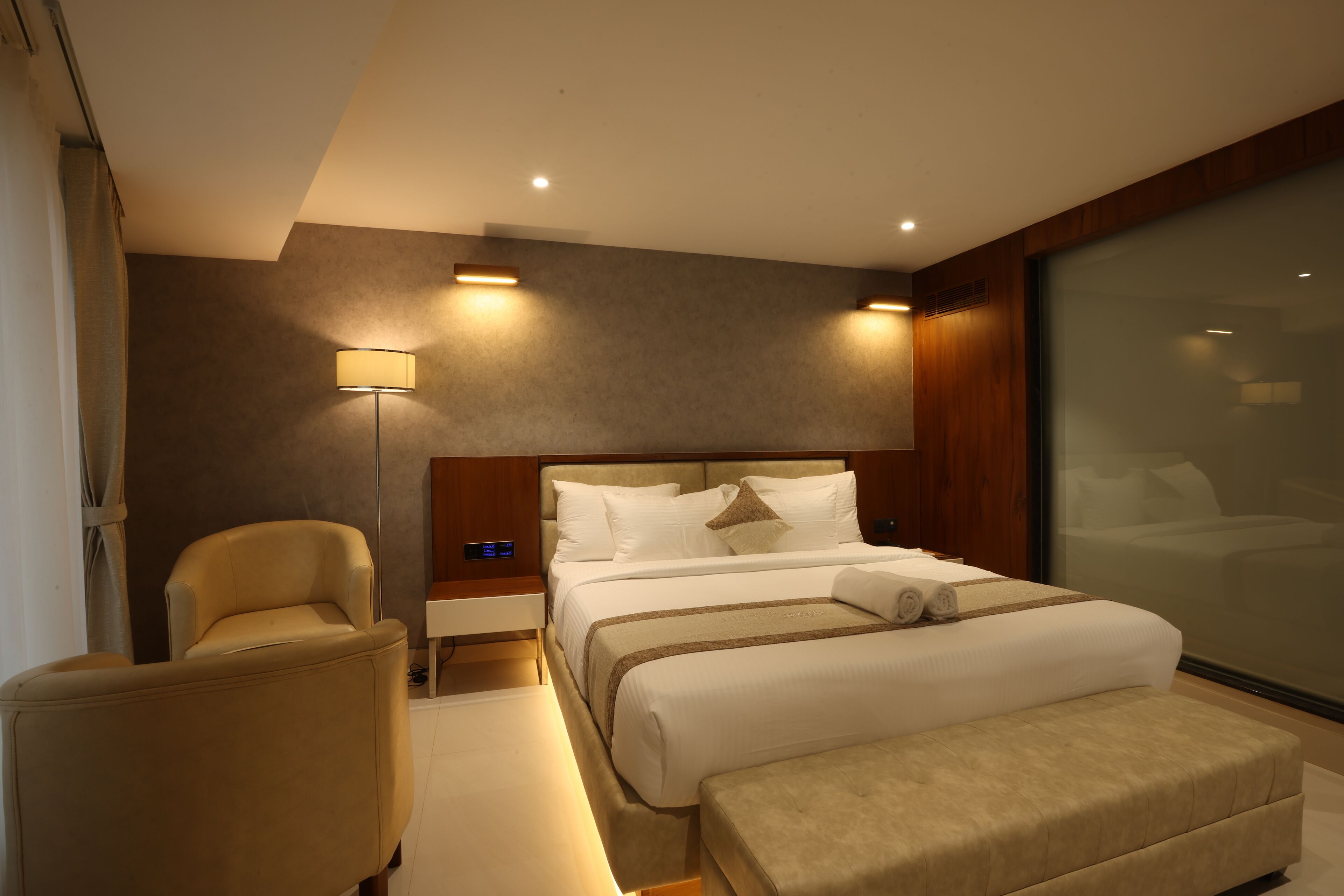 A modern hotel room with a large bed, a bedside table, a chair, and a large window.
