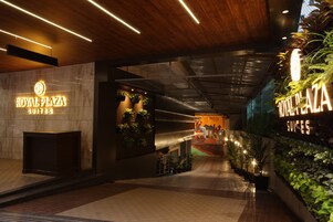 La entrada de Royal Plaza Suites, con un diseño moderno, presenta un techo de madera, señalización iluminada y plantas de interior.