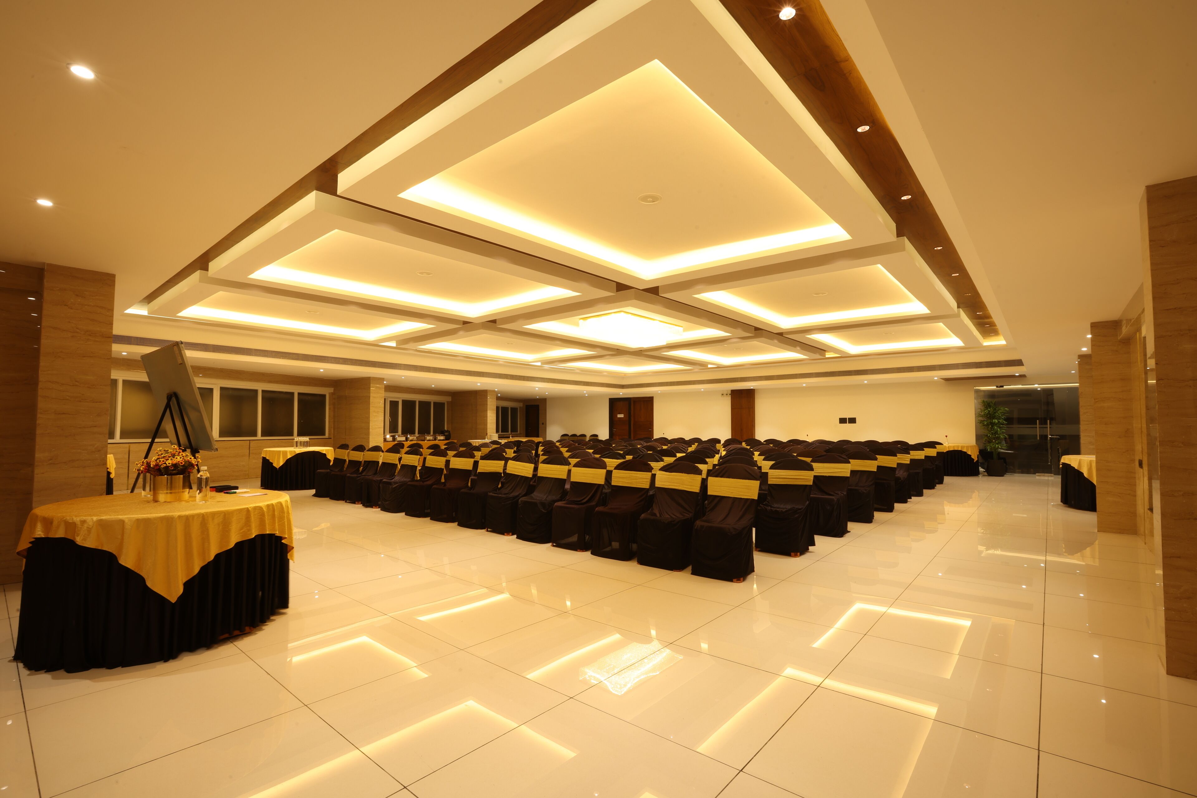 A spacious hall with rows of black chairs, a central table with a yellow tablecloth, and recessed ceiling lighting.