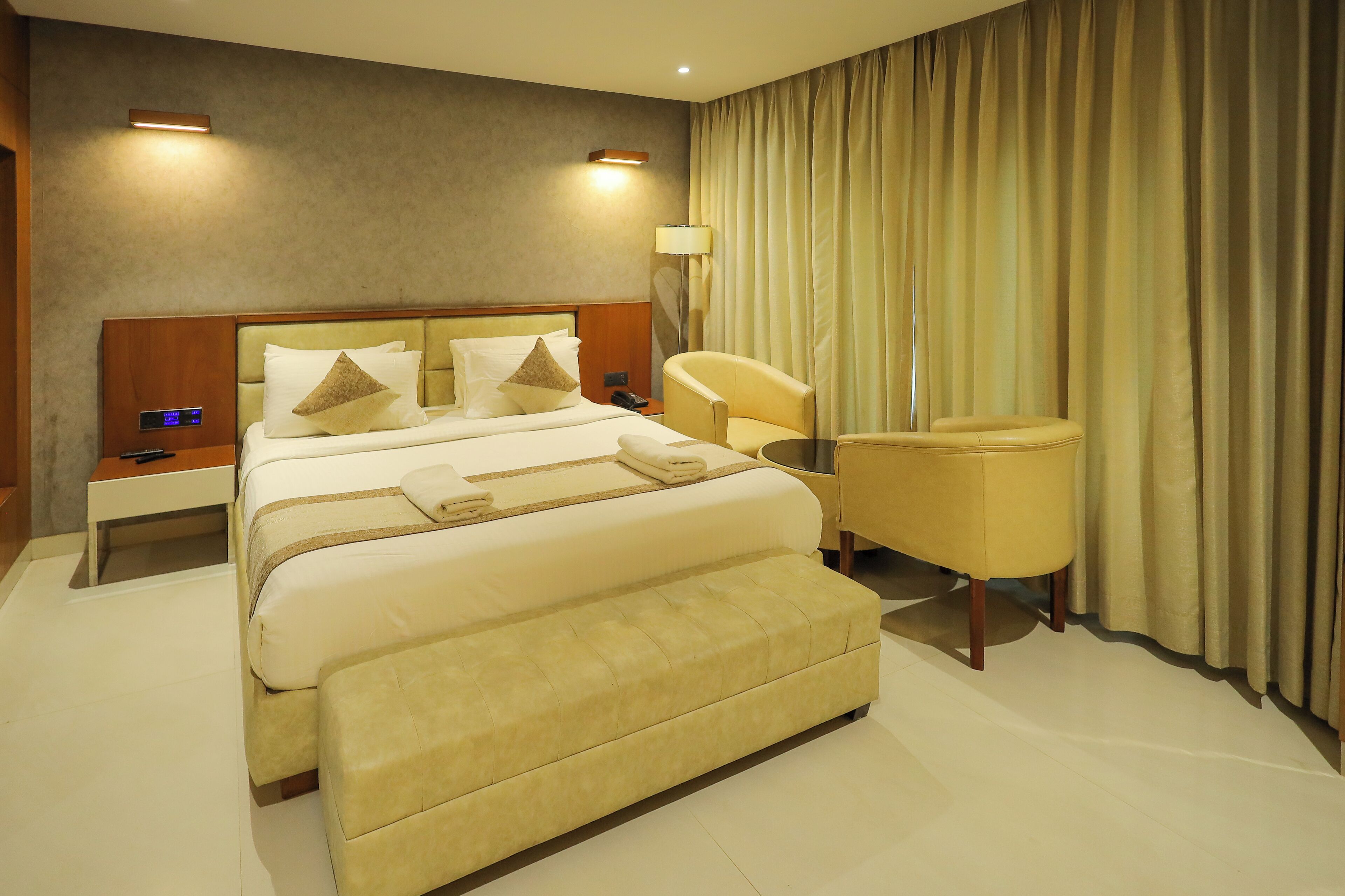 A hotel room with a large bed, a bedside table, a chair, and a lamp.