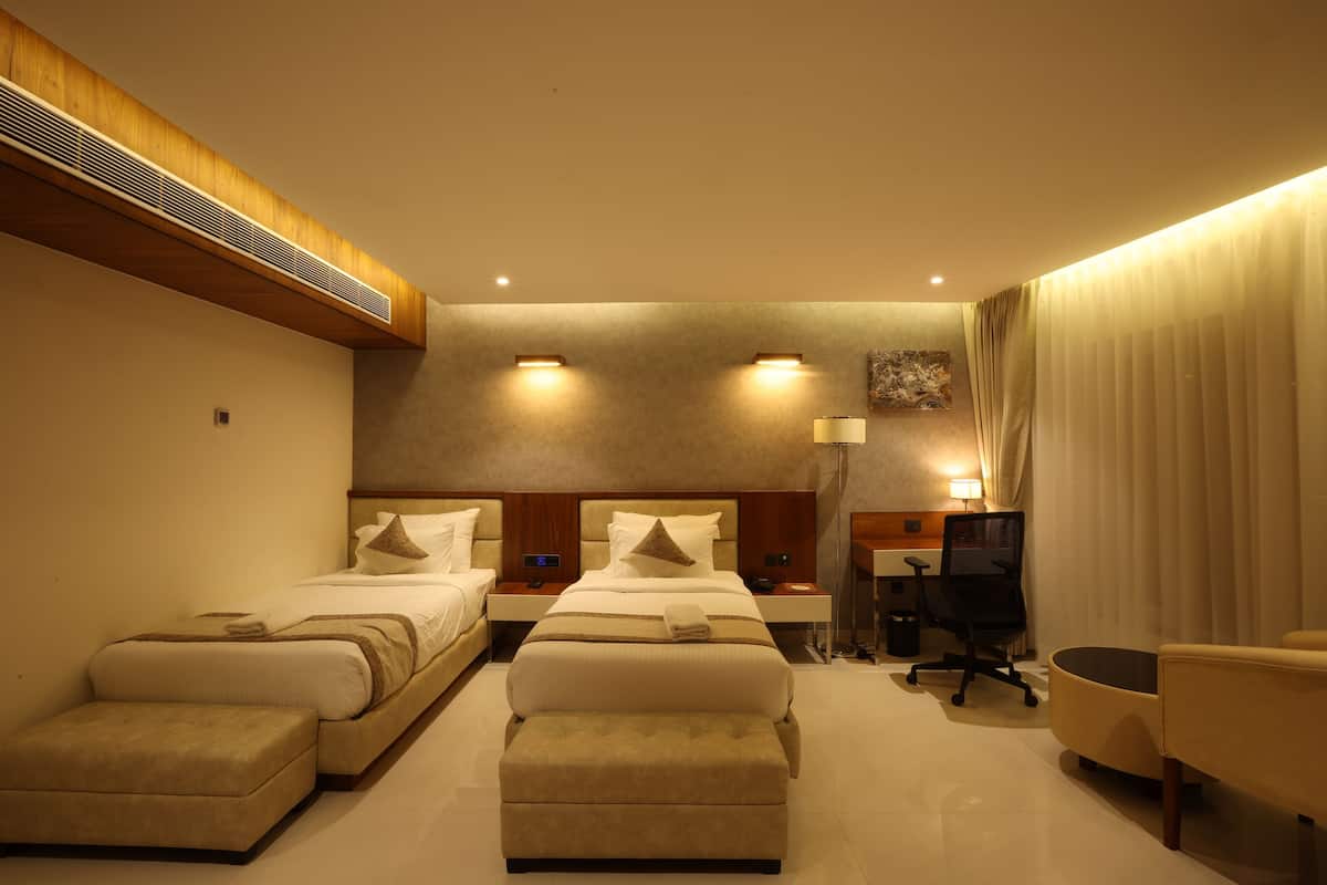 A hotel room with two beds, a desk, a chair, and a trash bin.