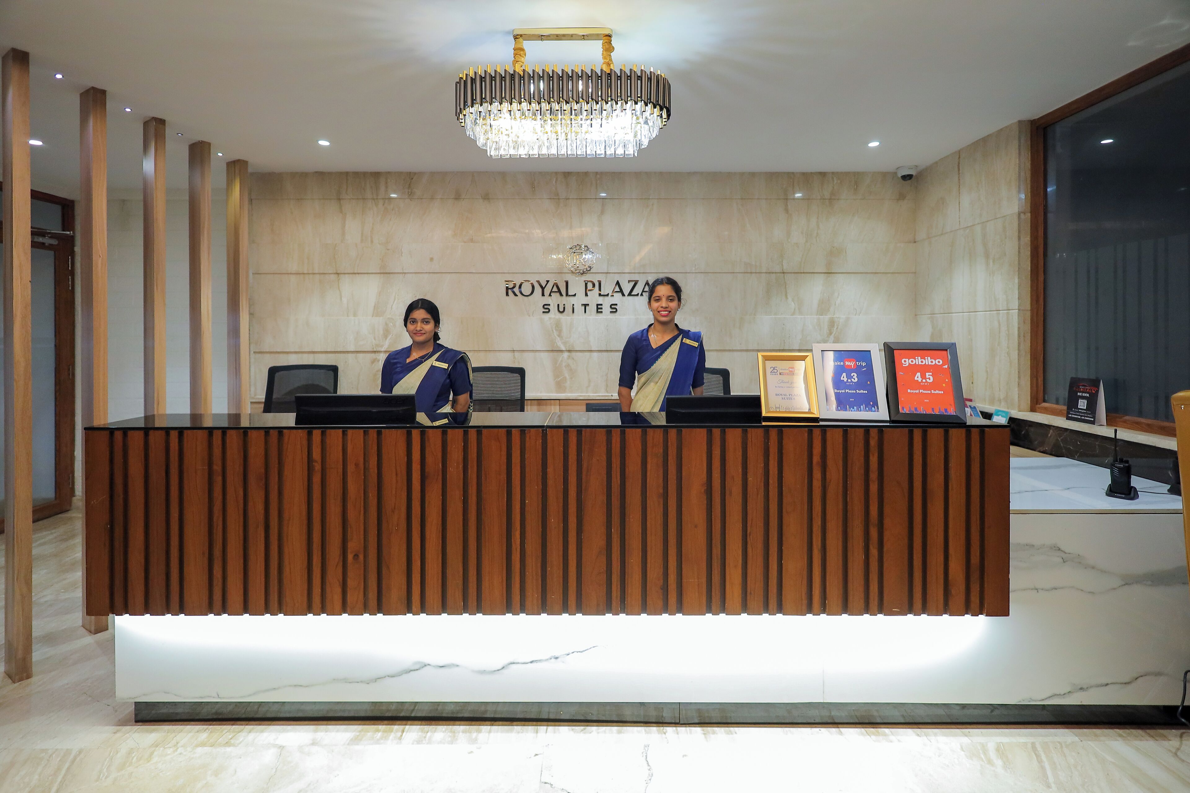 Balcão de recepção do Royal Plaza Suites, com piso de mármore, lustre e prêmios emoldurados.