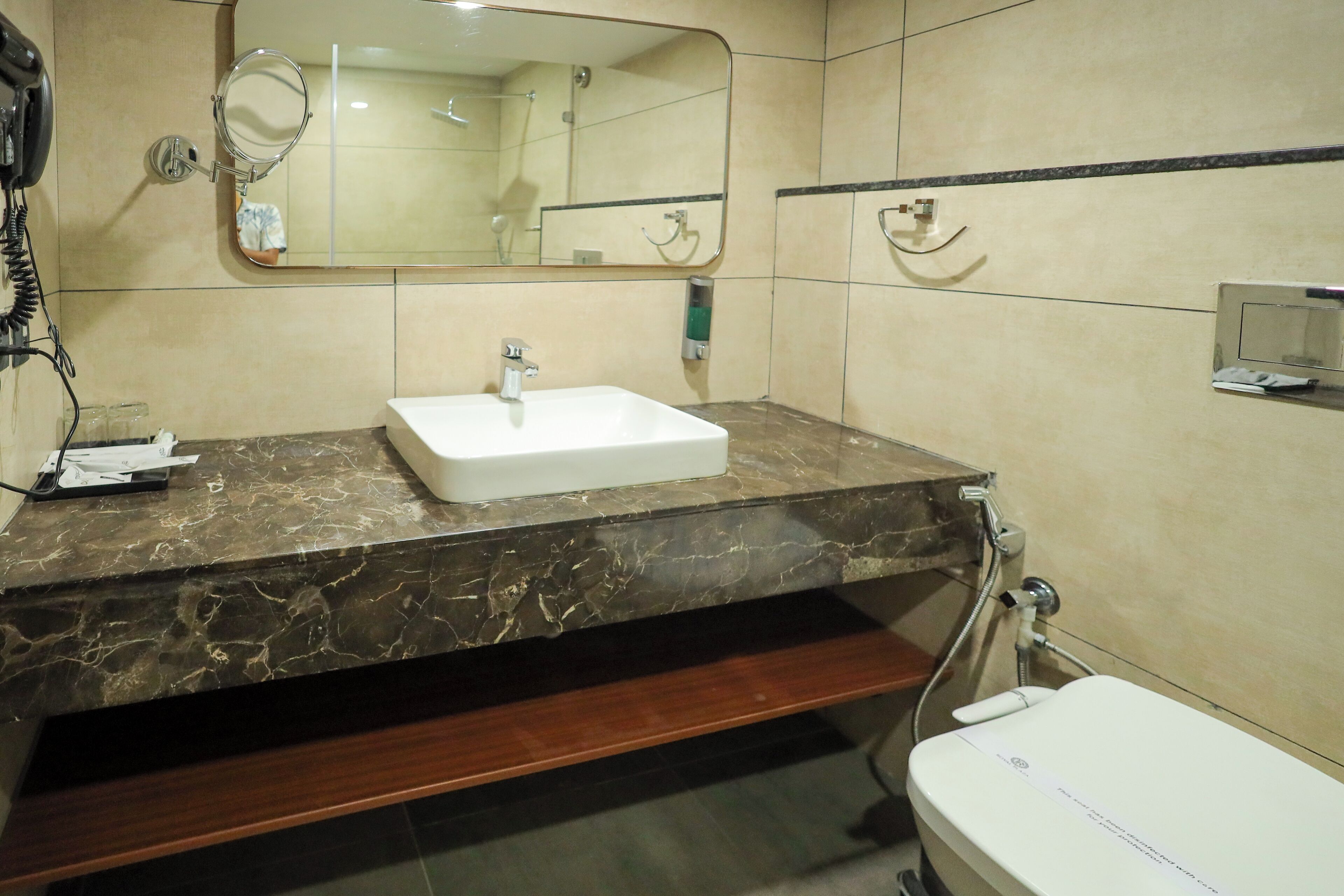 Une salle de bain avec un lavabo en marbre, un miroir, une douchette et des toilettes.