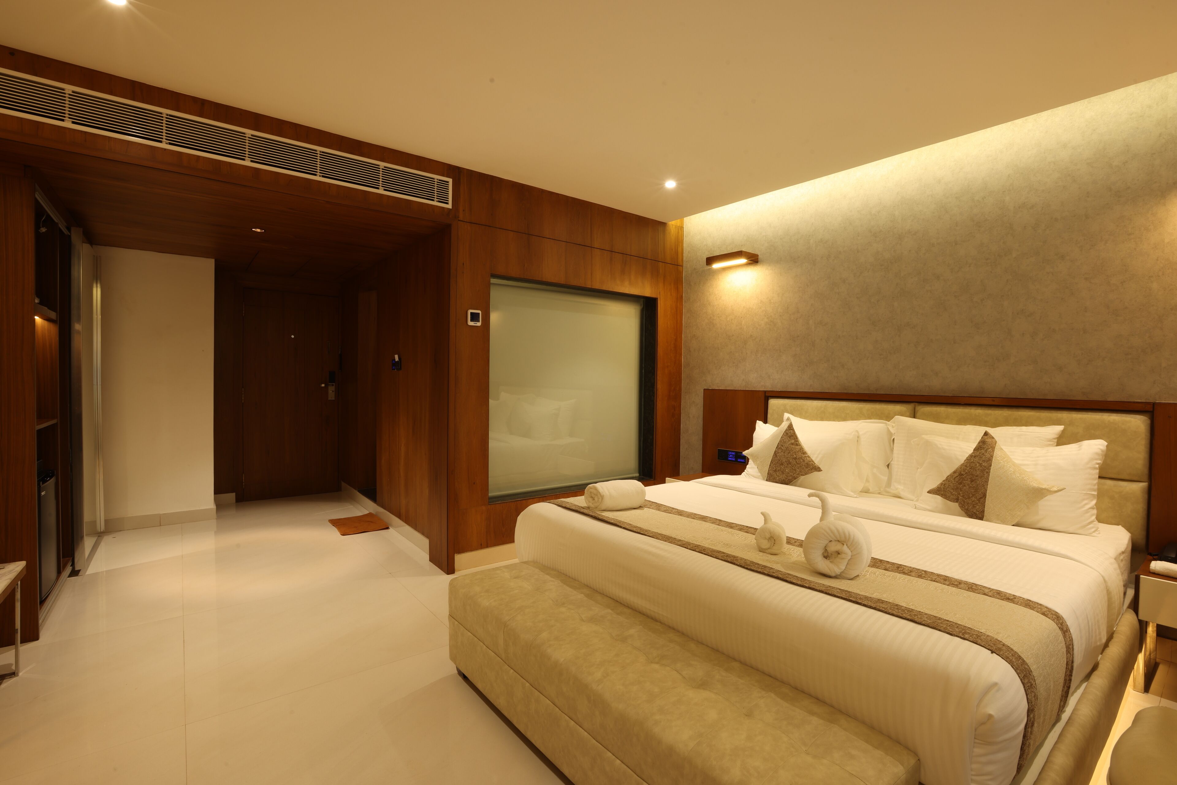 A modern hotel room with a large bed, a bedside table, a built-in TV, and a large window.