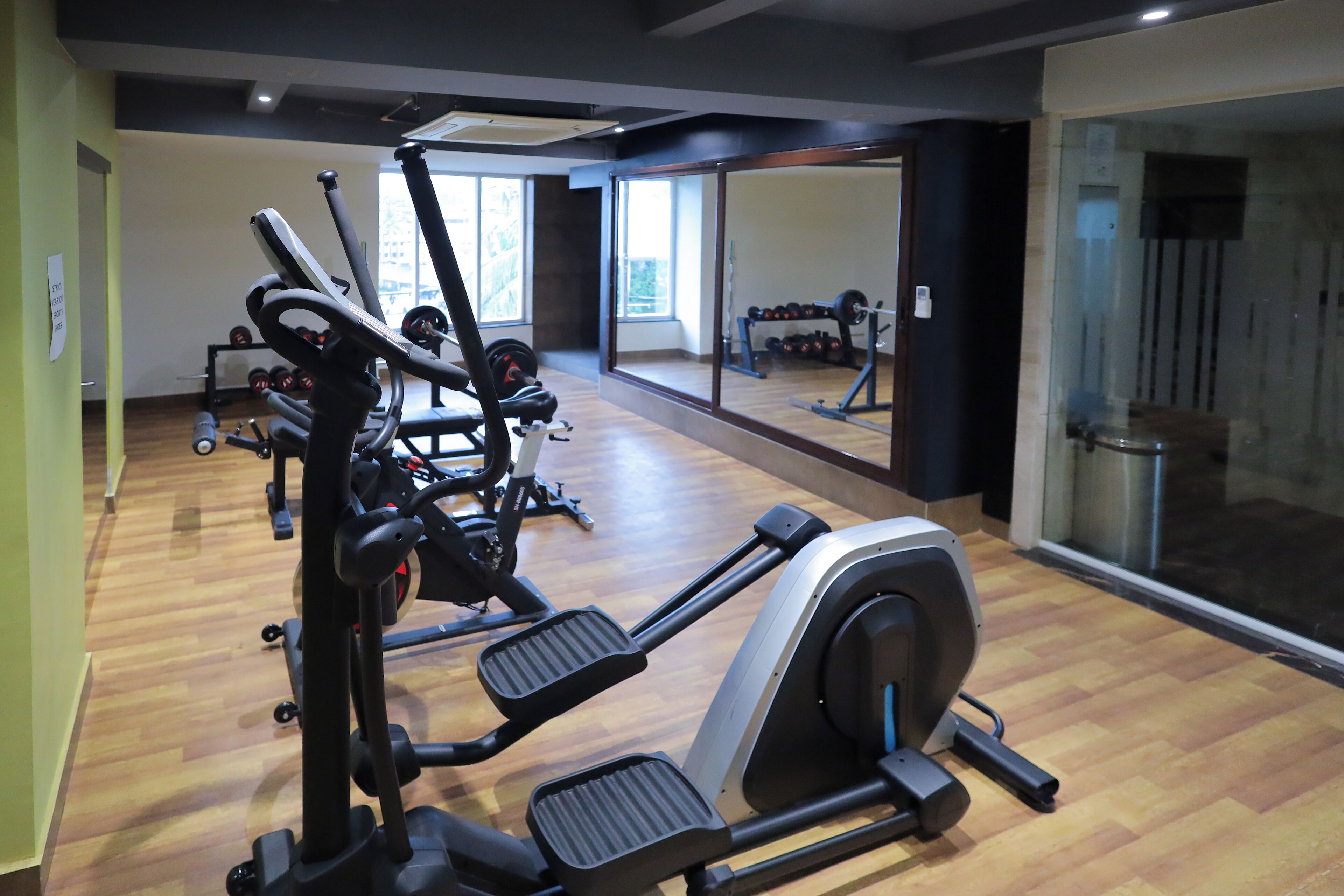 Un gimnasio con equipo de ejercicio, ventanas amplias y un espejo.