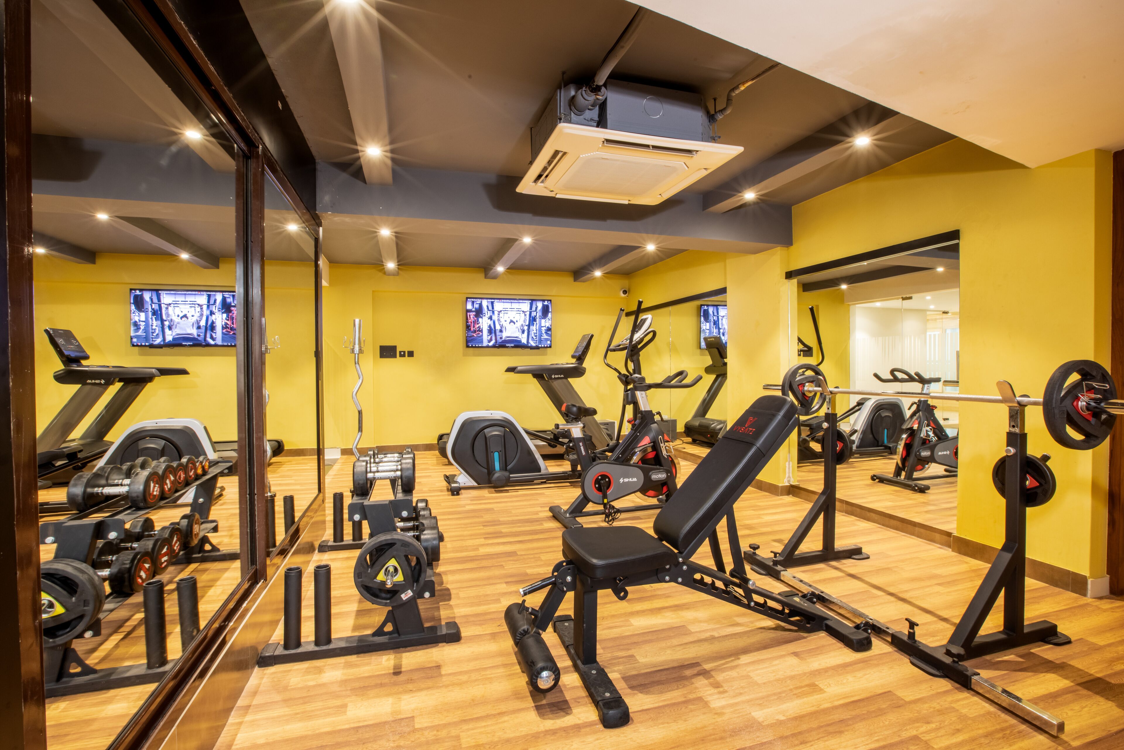 Un gimnasio con equipamiento de ejercicio, espejos y piso de madera.