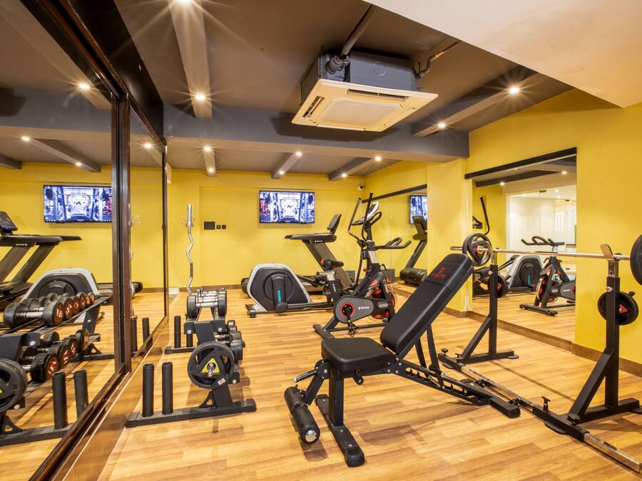 Un gimnasio con equipamiento de ejercicio, espejos y piso de madera.