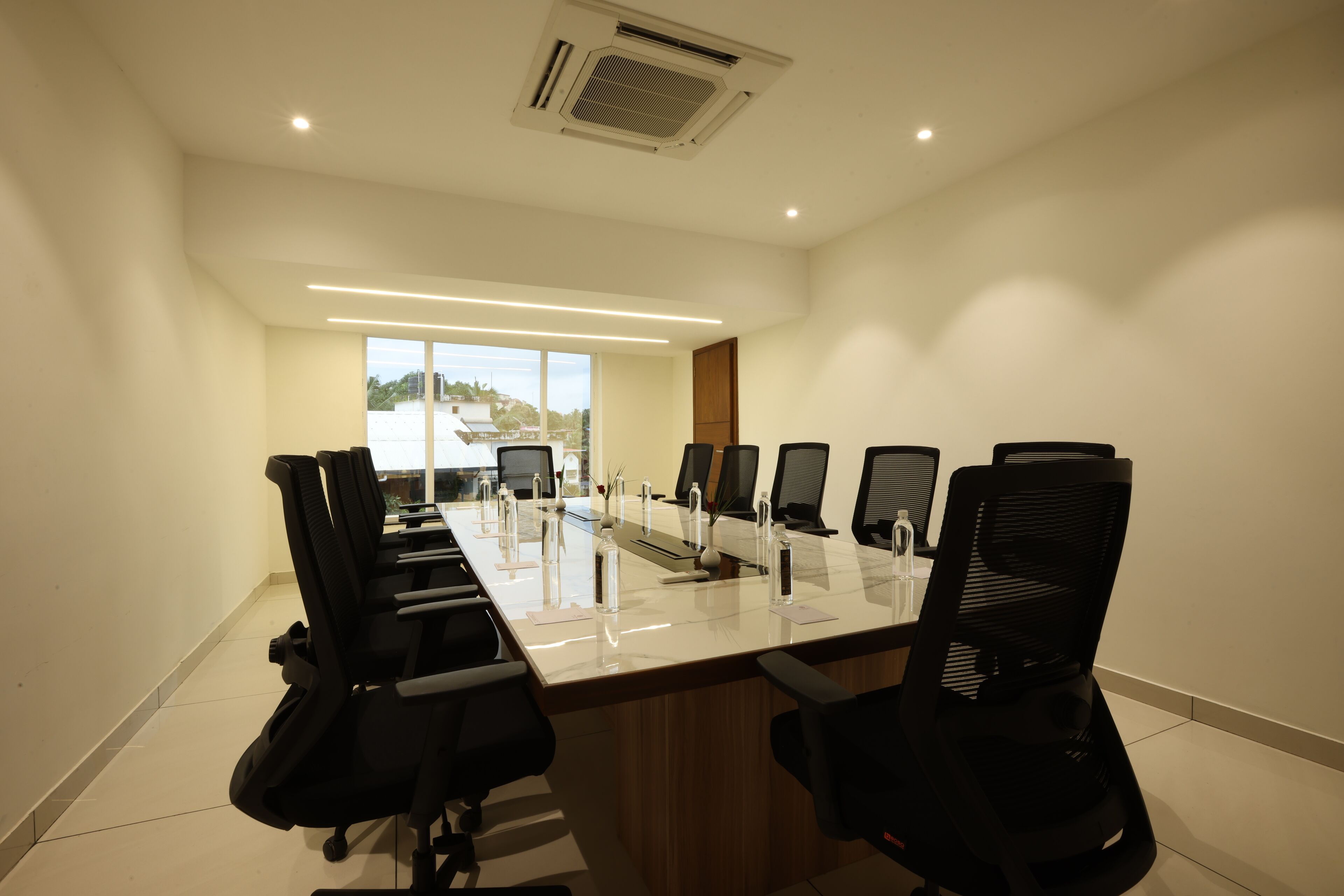 A conference room with a long table, black office chairs, and a view of buildings outside.