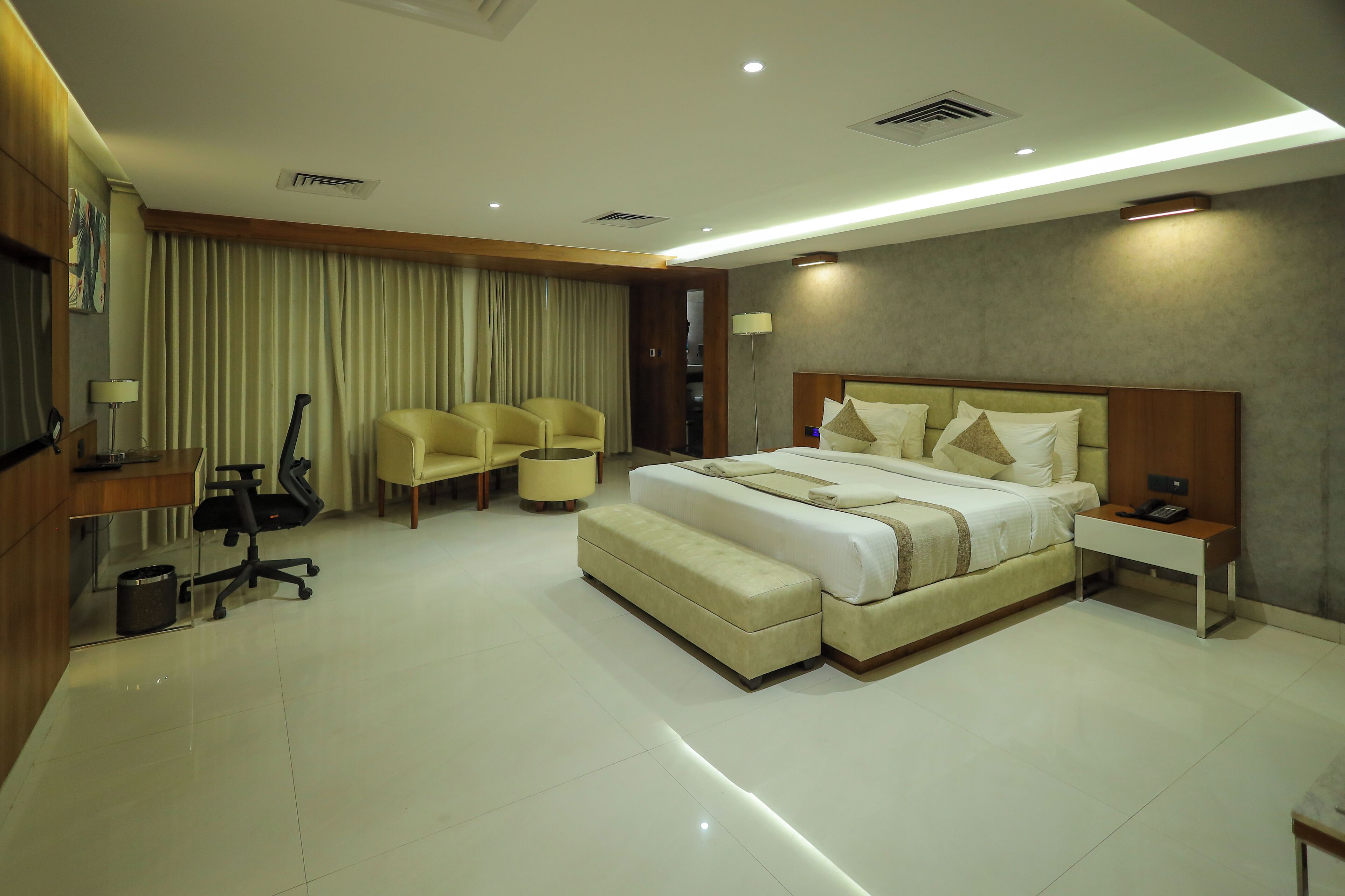 A hotel room with a large bed, two armchairs, a desk, and a lamp.