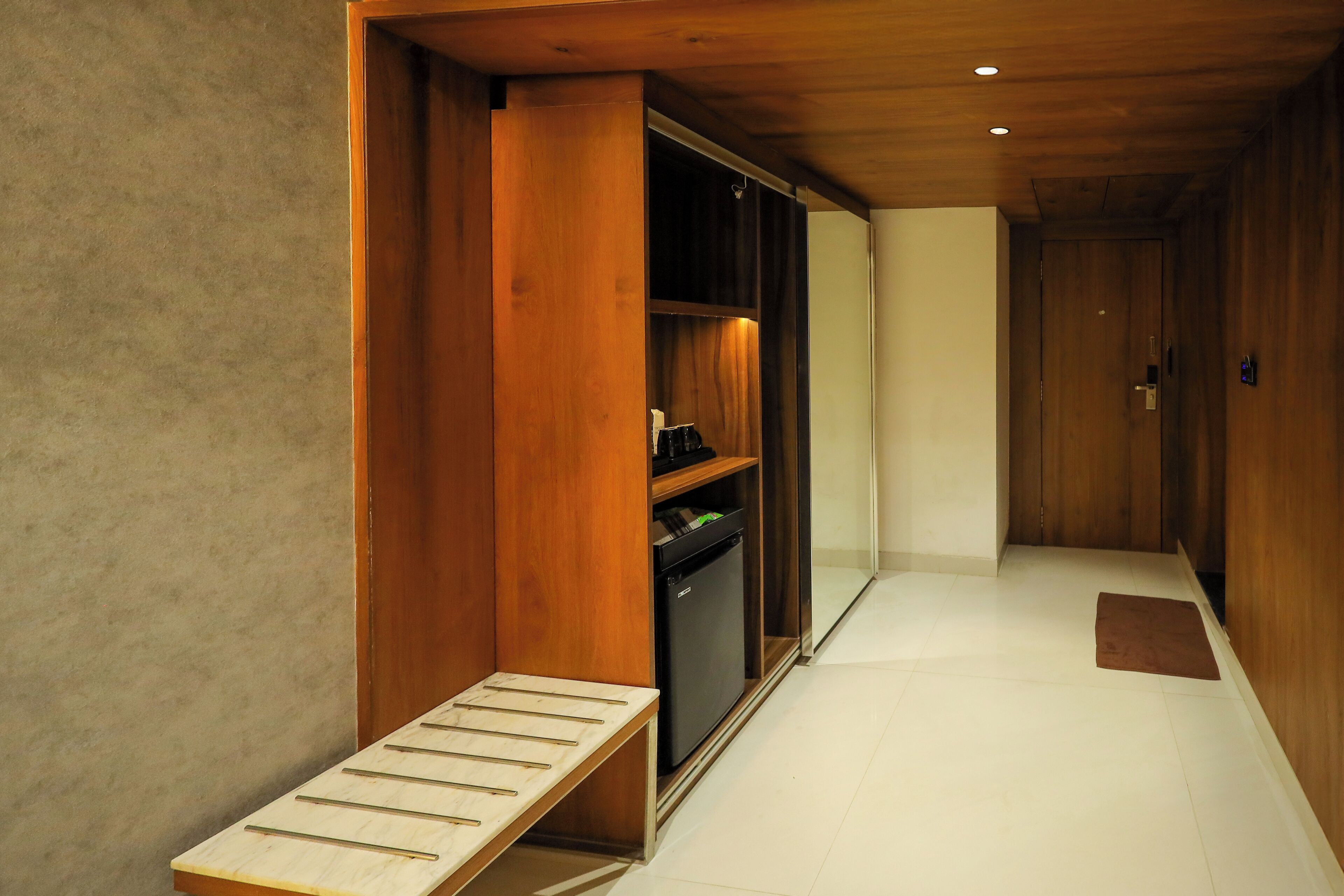Un pasillo con un banco de madera, un refrigerador empotrado y una puerta al final.