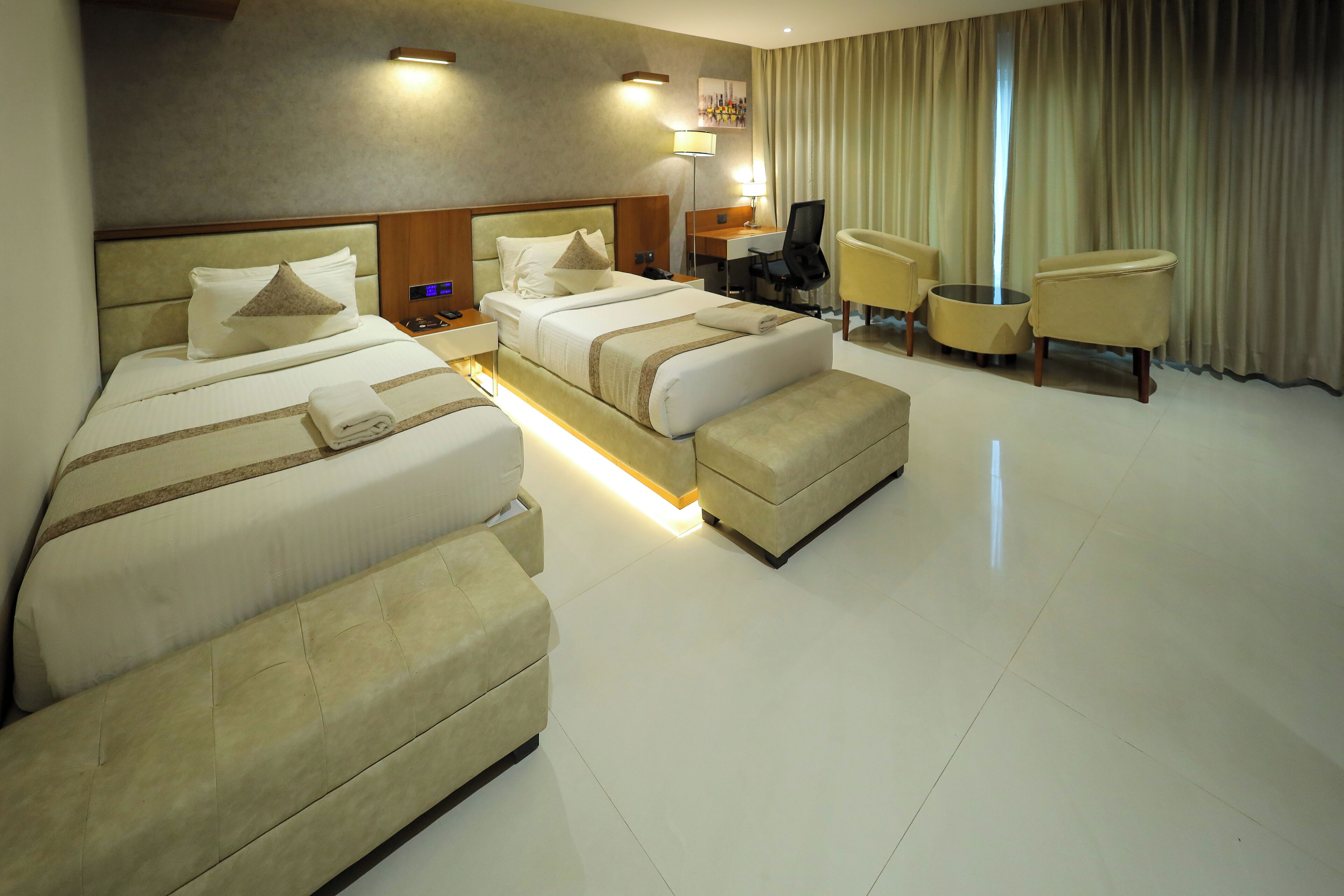 A hotel room with two beds, a desk, a chair, and a sofa.