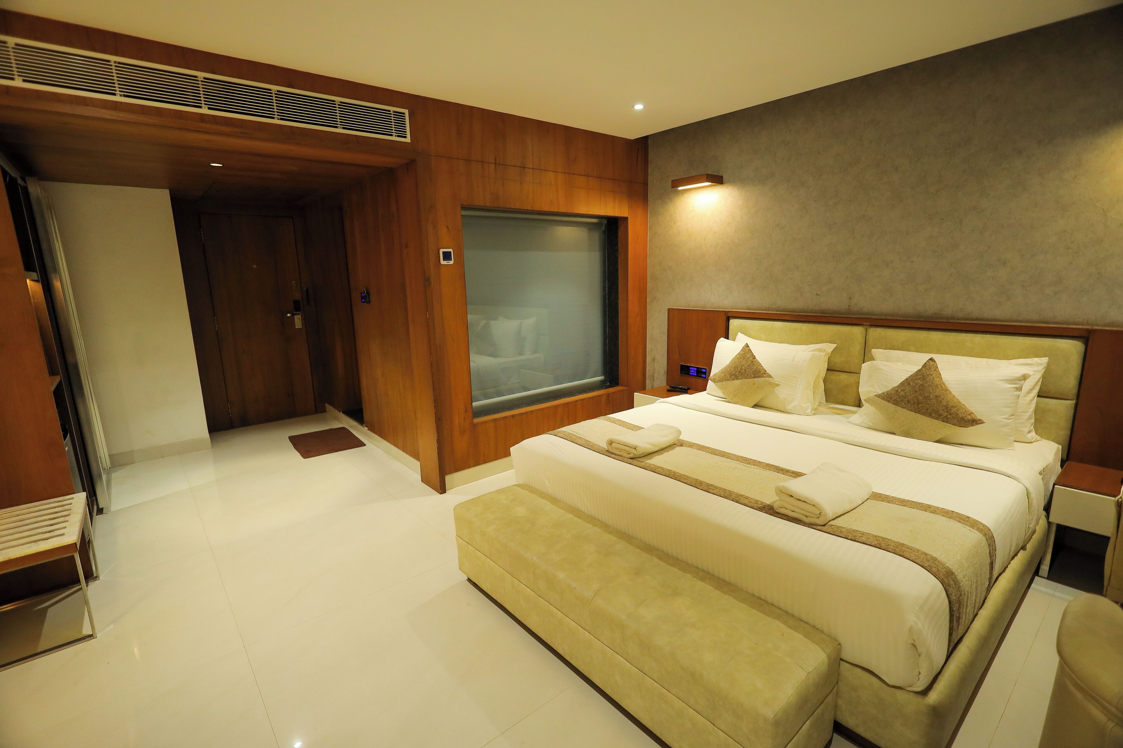 A modern hotel room with a large bed, a seating area, and a large window.