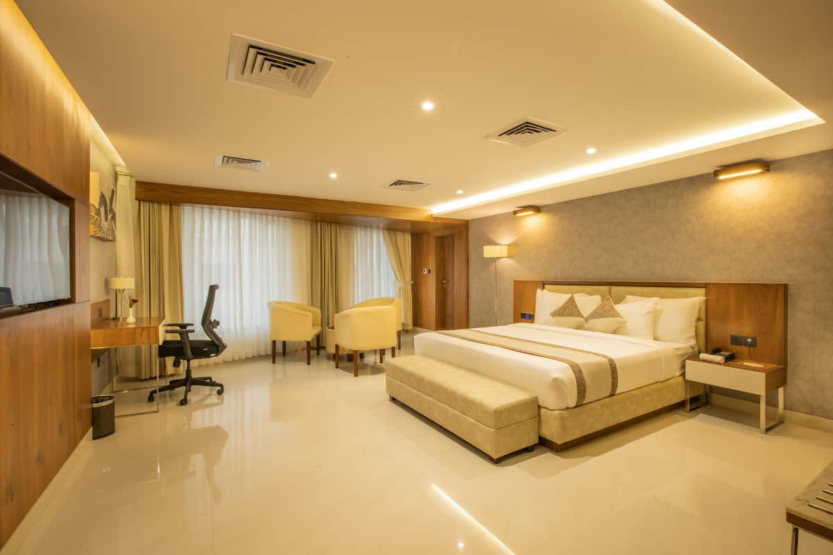 A modern hotel room with a large bed, a desk, two chairs, a bedside table, and a TV.