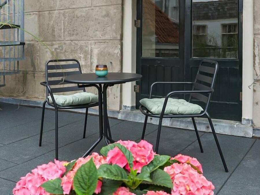An outdoor seating area with two metal chairs and a small round table, surrounded by pink flowers.