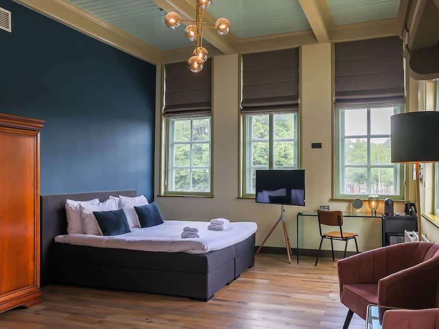 A bedroom with a large bed, a desk, a chair, and a wardrobe.