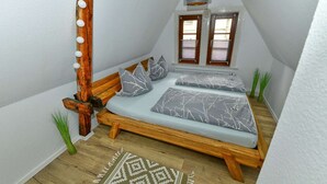 Una camera da letto accogliente e intima con un letto in legno, biancheria a motivi grigi, un lampadario e vista all'esterno attraverso una finestra con persiane.