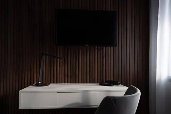 A modern room with a flat-screen TV mounted on a wooden wall, a white desk with a lamp, and a chair. - Hotel Cristal (Cluj-Napoca)