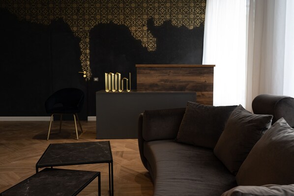 A modern living room with a dark sofa, a small table, and a reception desk. - Hotel Cristal (Cluj-Napoca)