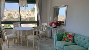 Una sala de estar con una mesa de centro de vidrio, un sofá color turquesa y un comedor con una mesa redonda y sillas.
