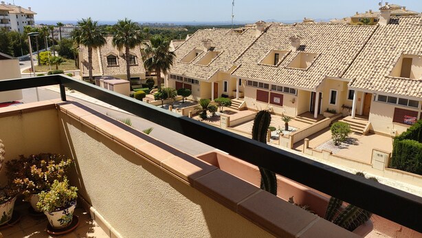 Un barrio residencial con tejados de tejas color terracota, un balcón con plantas en macetas y una vista despejada del mar al fondo.