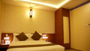 A hotel room with a large bed, bedside lamps, a nightstand, a mirror, and a small table with a vase of flowers. - DCHANDELIER (Kanayannur)