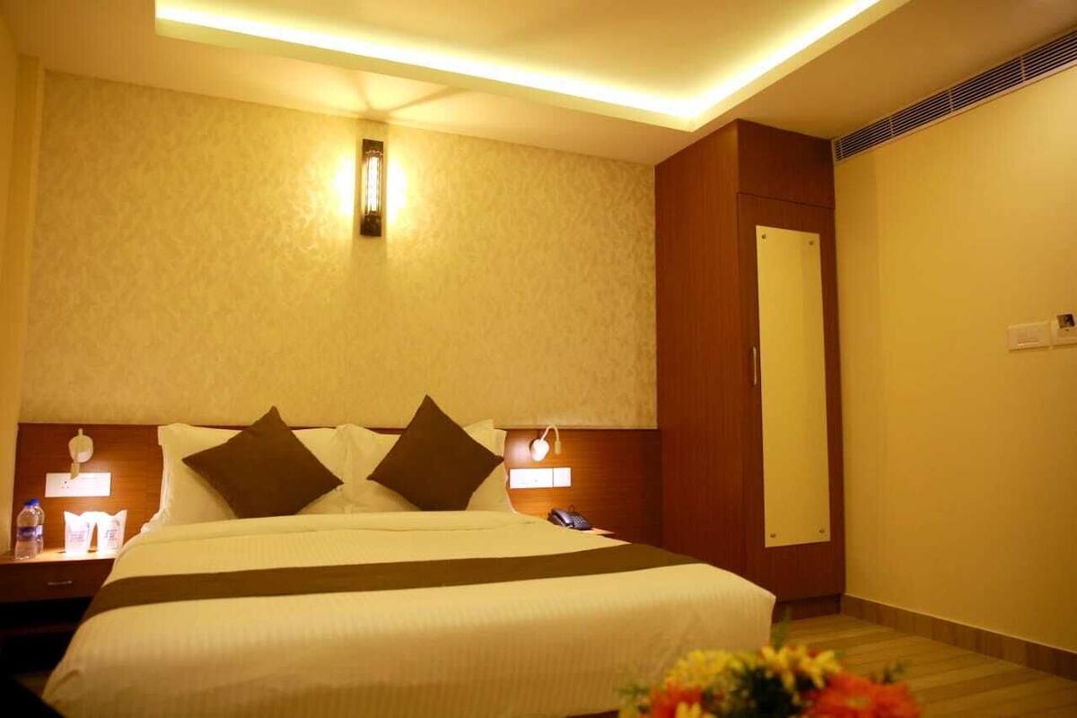 A hotel room with a large bed, bedside lamps, a nightstand, a mirror, and a small table with a vase of flowers.