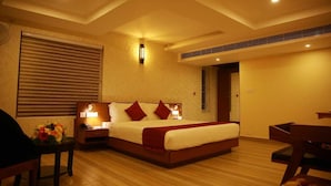 A hotel room with a large bed, bedside tables with lamps, a wooden floor, and a window with blinds. - DCHANDELIER (Kanayannur)