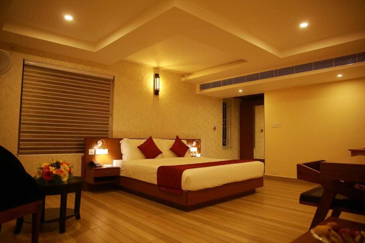 A hotel room with a large bed, bedside tables with lamps, a wooden floor, and a window with blinds.