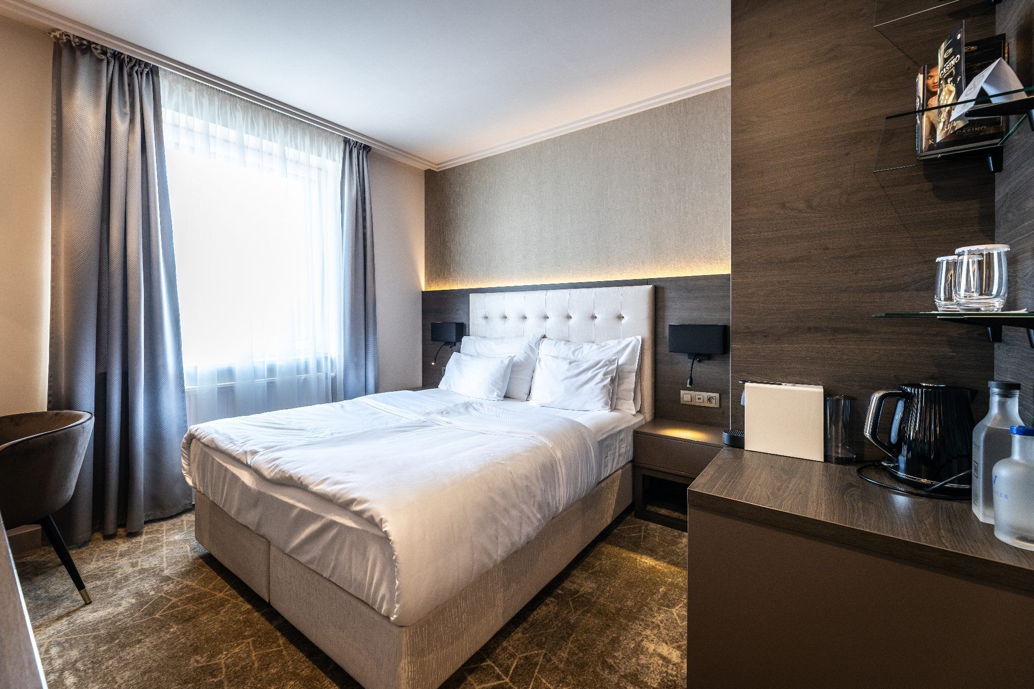 Habitación de hotel con una cama grande, un escritorio con cafetera y un estante con vasos y una botella.