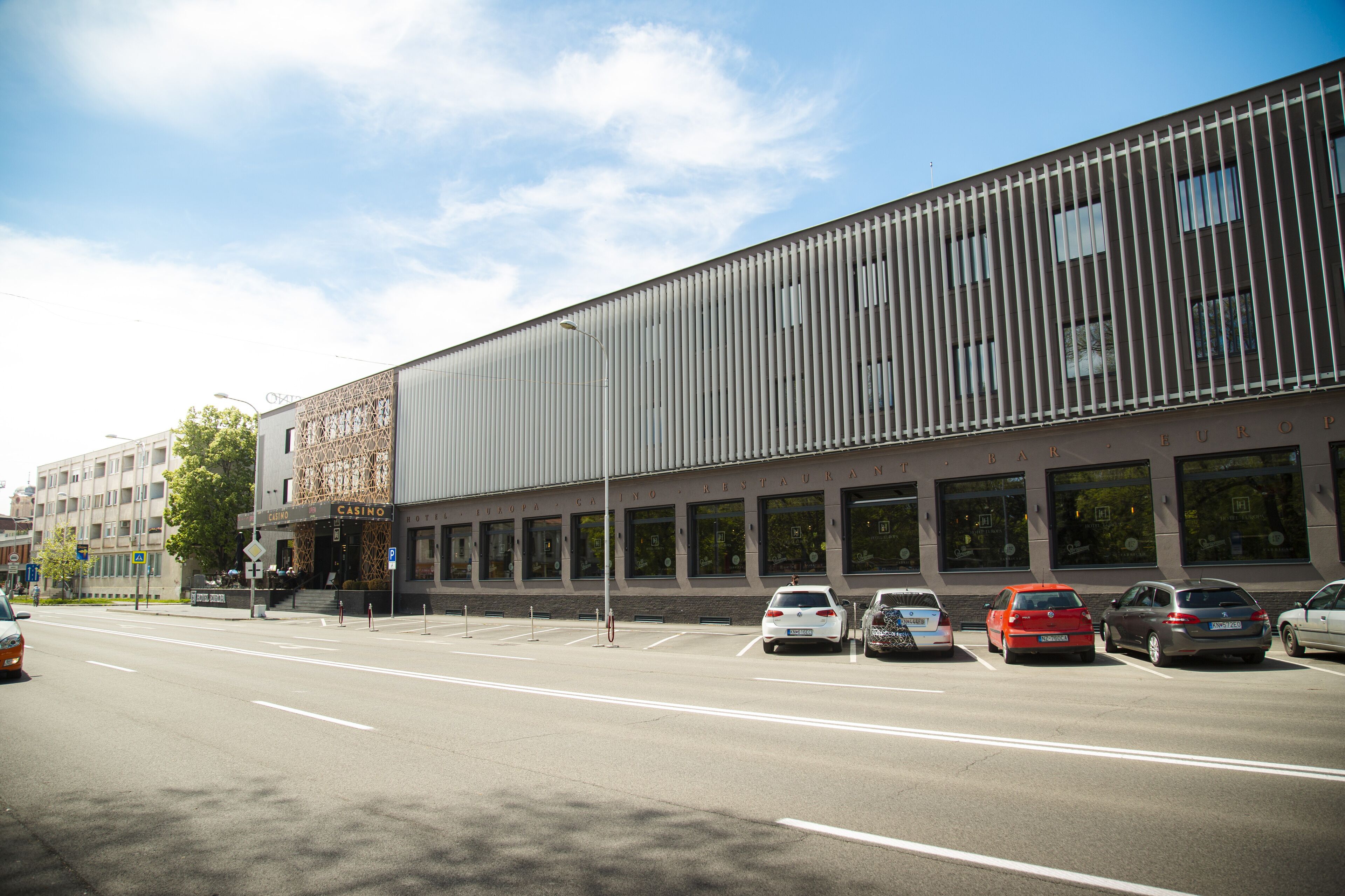 A modern building with a casino on the ground floor, featuring a large parking lot with several cars.