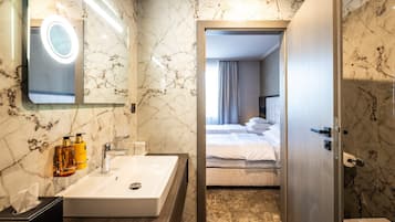 A hotel bathroom with a marble sink, a mirror with a light, and toiletries.