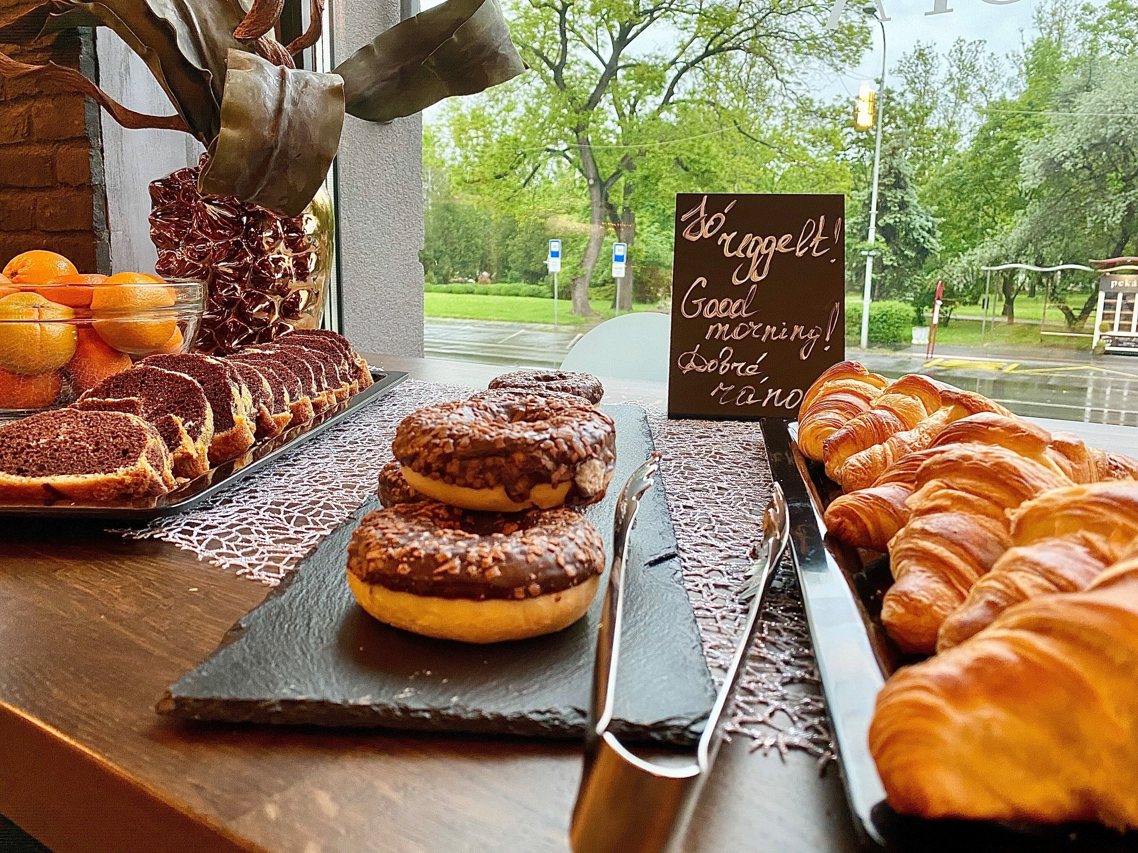 A breakfast buffet with pastries, fruits, and a sign greeting customers.