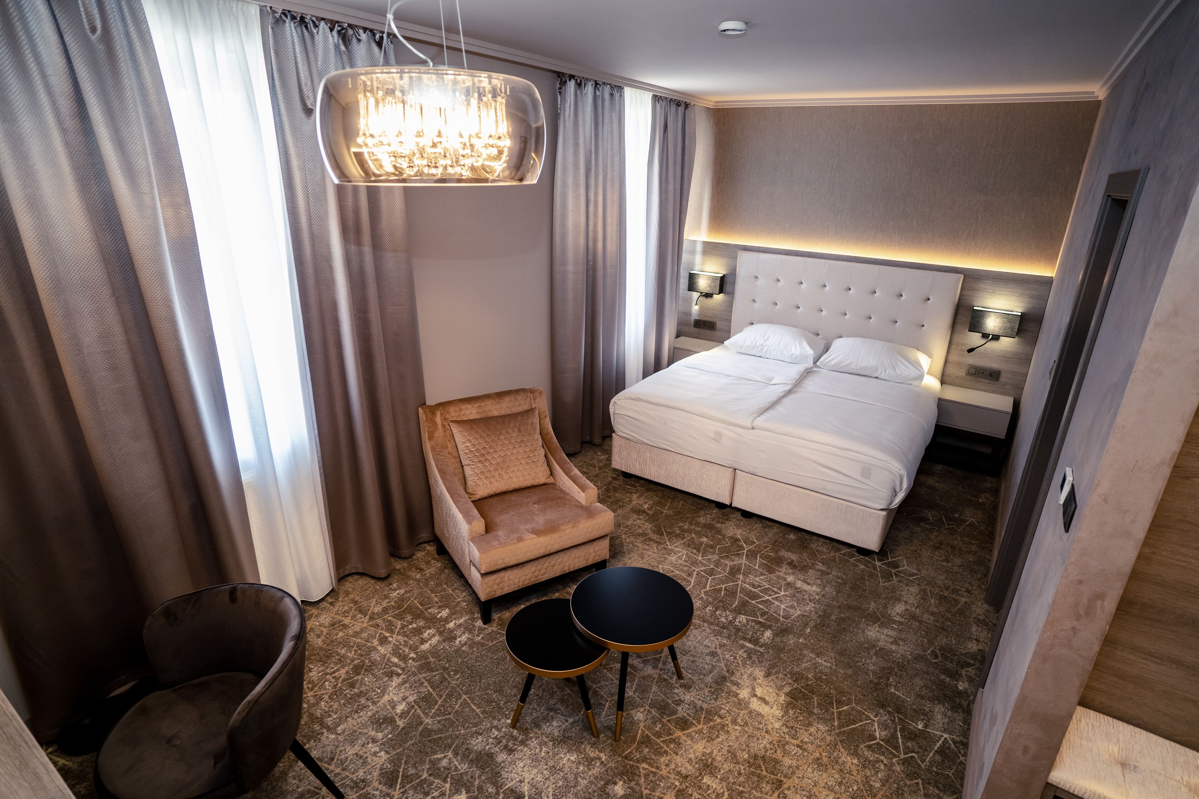 A hotel room with a large bed, a chair, two side tables, and a chandelier.