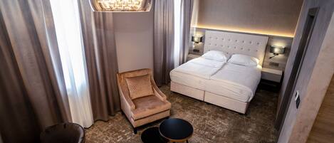 A hotel room with a large bed, a chair, two side tables, and a chandelier.