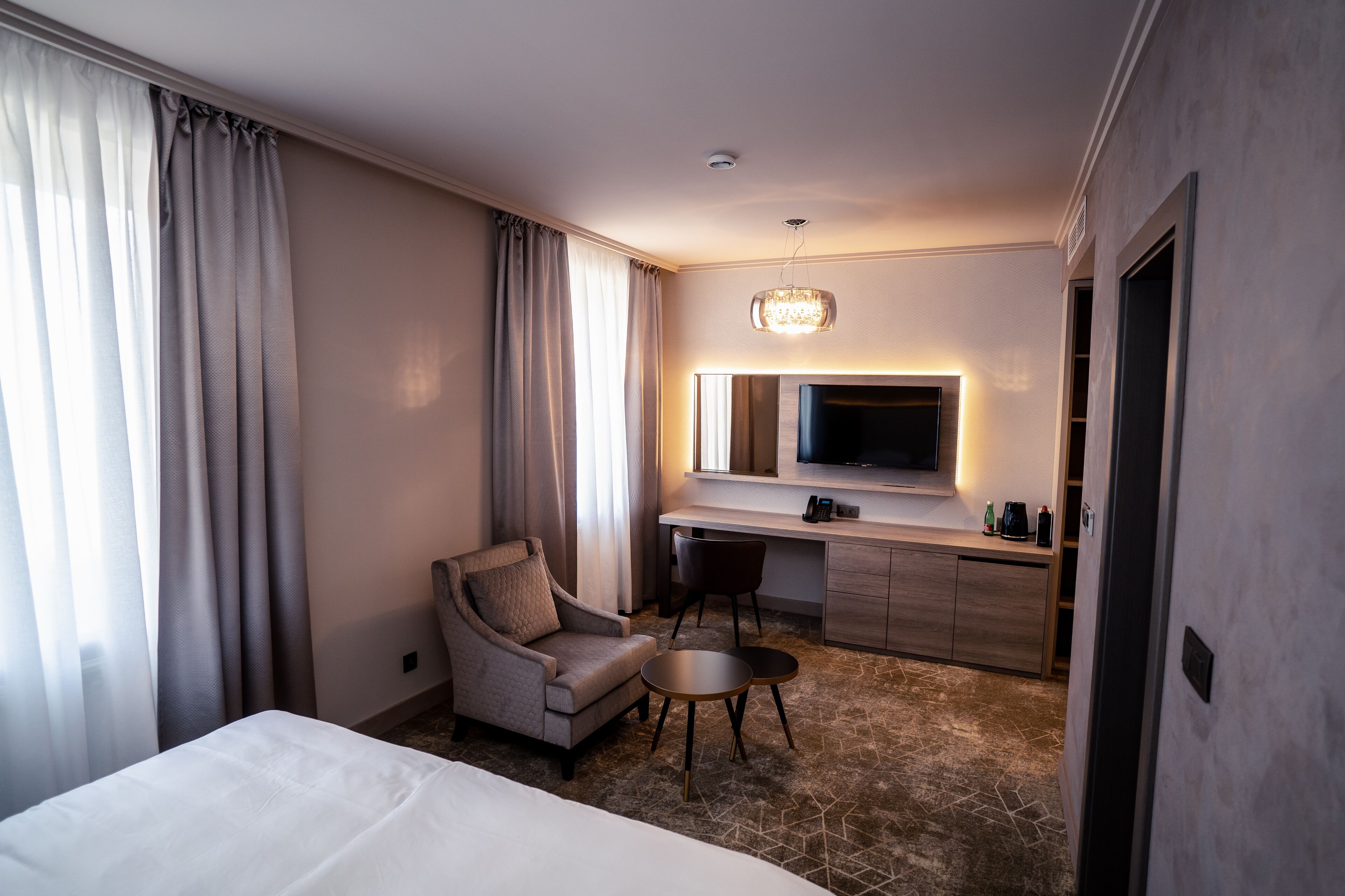 A hotel room with a bed, a desk, a chair, a TV, and a minibar.