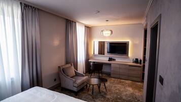 A hotel room with a bed, a desk, a chair, a TV, and a minibar.