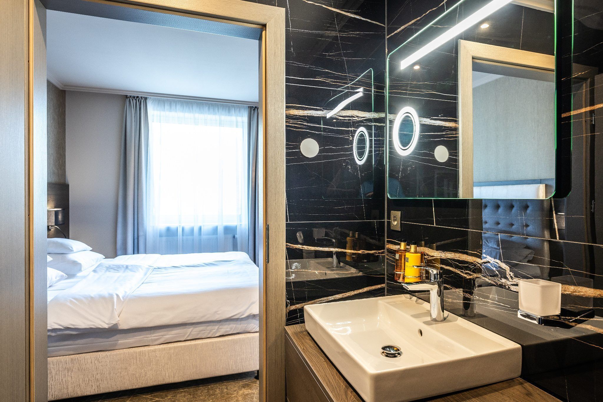 Une chambre d’hôtel avec un lit, un grand miroir, un lavabo et une fenêtre avec des rideaux.