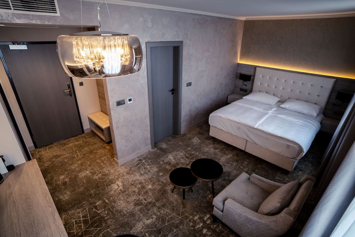 A modern hotel room with a large bed, a sitting area with two chairs, a small table, and a unique chandelier.