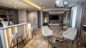 A modern living room with a bar area, comfortable seating, a flat-screen TV, and a chandelier.
