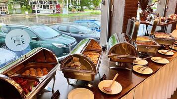 Disposição de buffet com diversos alimentos e vista para carros estacionados lá fora.